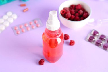 Boğaz ağrısı için sprey, haplar ve ahududu rengi arka planda, yakın plan