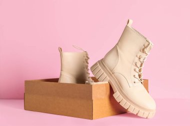 Pembe arka planda şık çizmeleri olan karton kutu.