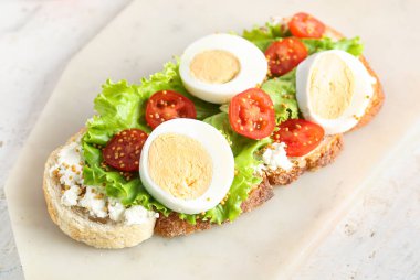 Hafif arka planda haşlanmış yumurta ve domatesli lezzetli tost tahtası, yakın plan.