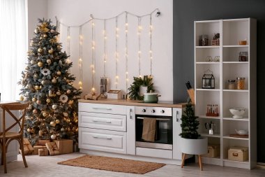 Mutfağın içinde Noel ağaçları, parlayan ışıklar ve beyaz tezgahlar var.