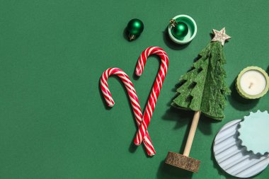 Podyumları, mumu, bastonu ve topları yeşil arka planda olan dekoratif Noel ağacı.