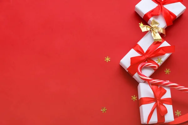 赤い背景にクリスマスプレゼントとお菓子の杖で構成 — ストック写真
