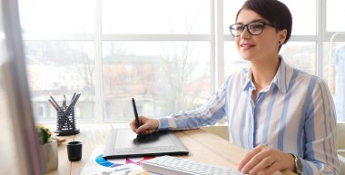 Genç bayan tasarımcı ofiste bilgisayar üzerinde çalışıyor.