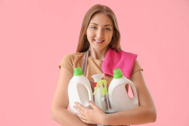 Pembe arka planda deterjan şişeleri olan genç bir kadın.