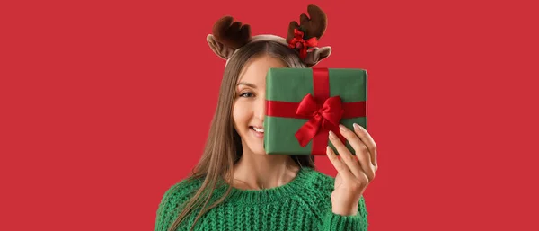 快乐的年轻女子 长着驯鹿角 背景是红色的圣诞礼物 — 图库照片