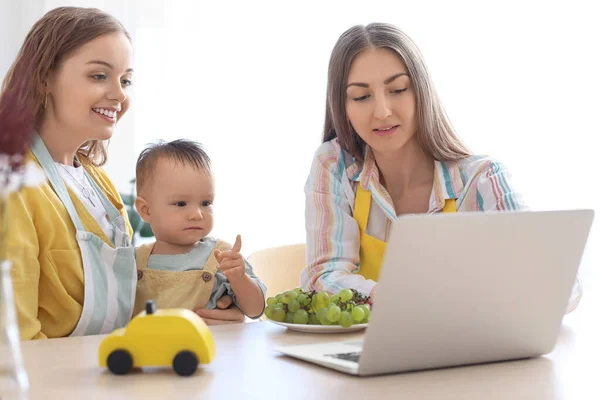 一对快乐的女同性恋夫妇带着他们的小宝宝和笔记本电脑坐在厨房的桌子上 — 图库照片