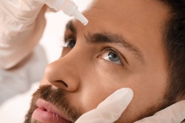 Oftalmolog, hastanede genç adamın gözüne damla damlatıyor.