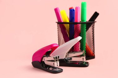 Keçeli kalemleri ve pembe arka planda zımbaları olan tutucu.