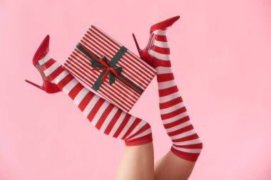 Pembe arka planda hediye kutusu olan Noel çoraplı bir kadın.