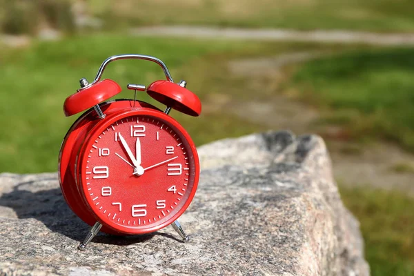 Red vintage alarm clock on stone in park, closeup
