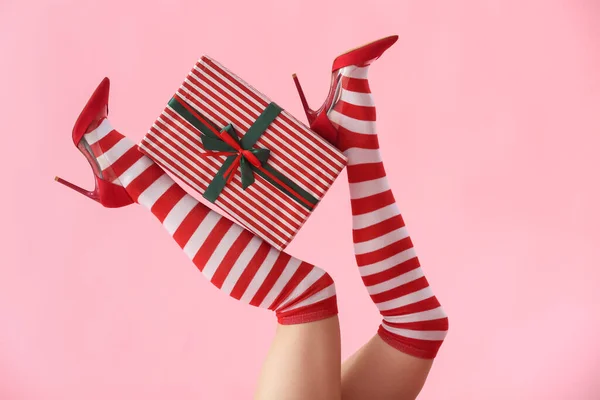 stock image Woman in Christmas stockings with gift box on pink background