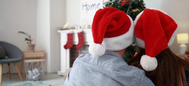 Happy young couple in Santa hats celebrating Christmas at home, back view clipart