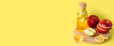 Bir şişe elma sirkesi ve sarı arka planda taze meyveler.