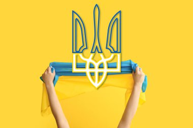 Ukrayna bayrağı ve sarı arka planda arması olan eller.