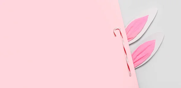 ピンクとグレーの背景にキャンディ杖と紙のウサギの耳 — ストック写真