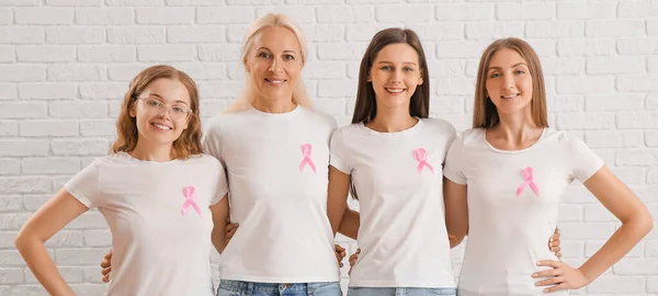 Beautiful women with pink ribbons on white brick background. Breast cancer awareness concept