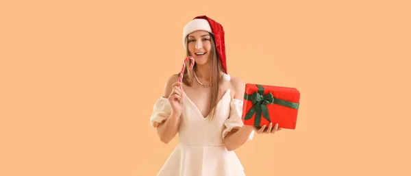 戴着圣诞礼帽 戴着米色背景的圣诞礼物和糖果的漂亮女人 — 图库照片