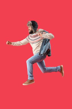 Sıcak şapkalı yakışıklı adam kırmızı arka planda zıplıyor.