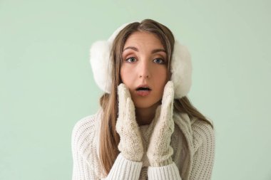 Yeşil arka planda sıcak kulak manşetleriyle ve eldivenleriyle şok olmuş genç bir kadın.