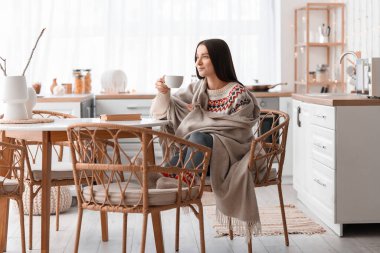 Mutfaktaki yemek masasında çay içen genç bir kadın.