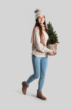 Gri arka planda küçük bir Noel ağacı olan kalın şapkalı genç bir kadın.