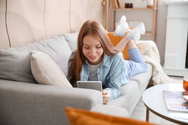 Evdeki gri koltukta tablet bilgisayar kullanan güzel bir kadın.