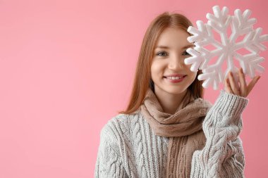 Pembe arka planda büyük kar taneleri olan, sıcak eşarplı, kızıl saçlı genç bir kadın.