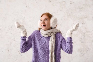 Hafif arka planda, sıcak kulaklık ve eşarp takan kızıl saçlı genç bir kadın.