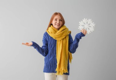 Gri arka planda büyük kar taneleri olan, sıcak eşarplı, kızıl saçlı genç bir kadın.