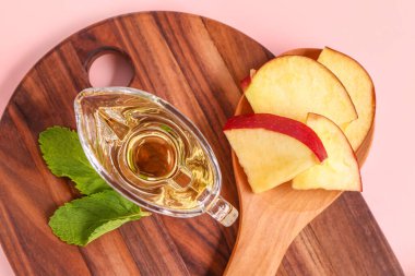 Elma sirkesi soslu ahşap tahta tahta tahta ve pembe arka planda meyveler, yakın plan.