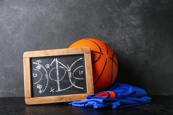 Chalkboard with drawn scheme of basketball game, uniform and ball on dark background
