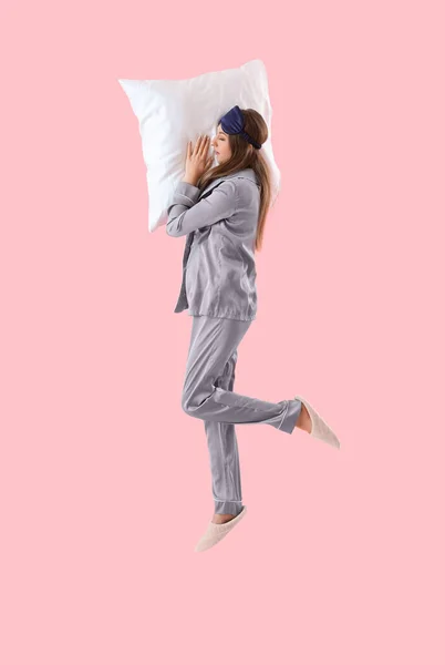 stock image Young woman in pajamas with pillow jumping on pink background