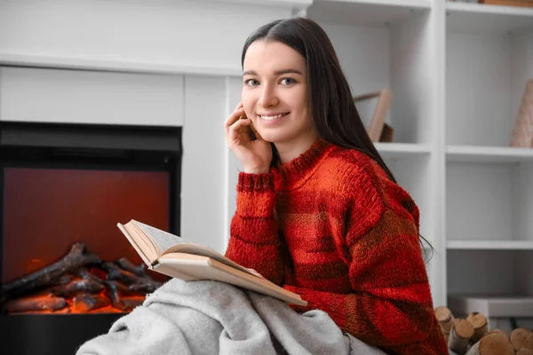 Ung Kvinde Varm Sweater Læsning Bog Nær Pejs Derhjemme - Stock-foto