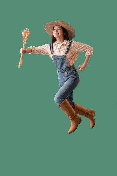 年轻的女农民带着小麦穗在绿色背景上跳跃 — 图库照片