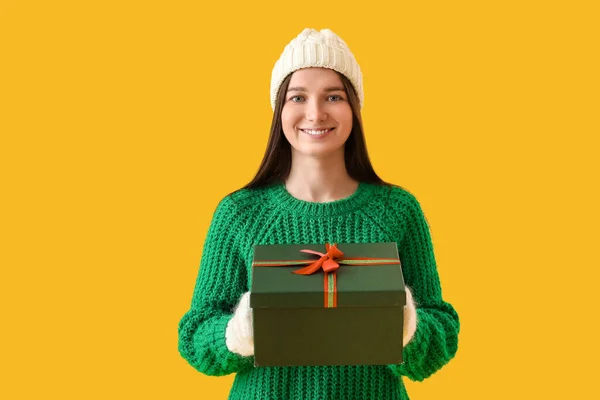 若いです女性で暖かいです帽子とともにクリスマスプレゼント上の黄色の背景 — ストック写真