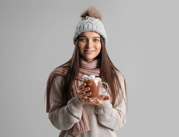 戴着温暖帽子 头戴玻璃杯可可和棉花糖 身披灰色背景的年轻女子 — 图库照片