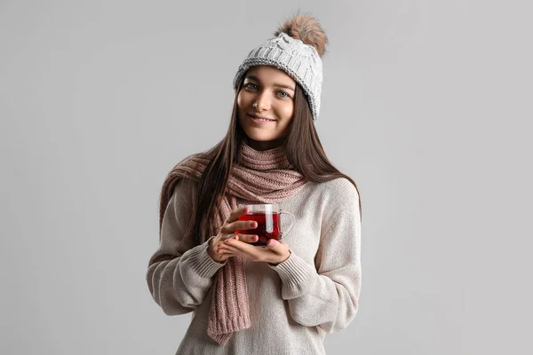 戴着温暖帽子 头戴灰色背景玻璃杯茶的年轻女子 — 图库照片