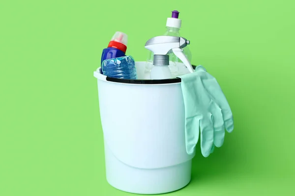 Bin with cleaning supplies on green background
