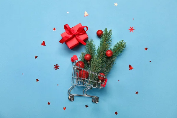 stock image Shopping cart with fir branches, Christmas balls and gift on blue background