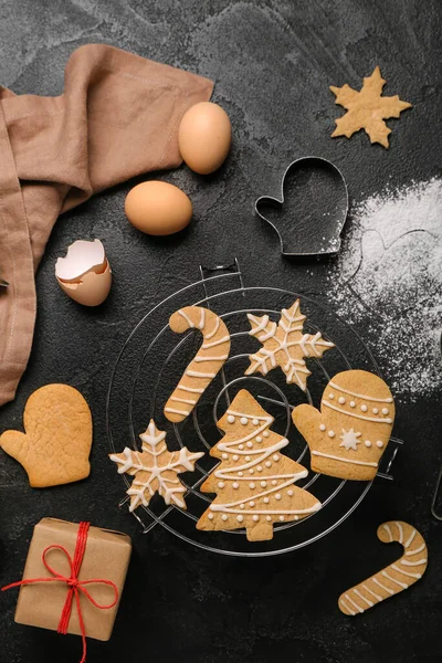 Grid with tasty Christmas cookies, ingredients and gift on dark background