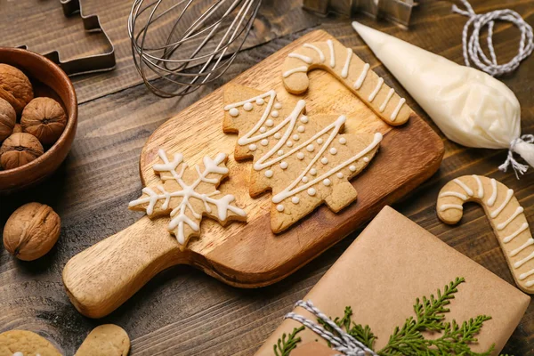 Board with tasty Christmas cookies, cream and gift on wooden background, closeup
