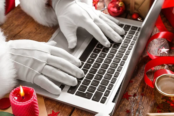 stock image Santa Claus using laptop on wooden table, closeup