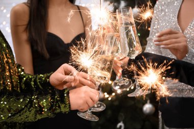 Şampanya bardakları ve Noel havai fişekleri olan güzel elbiseli genç kadınlar, yakın plan.