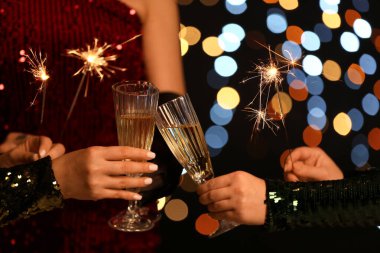 Zarif elbiseli, yanan maytaplı, bulanık Noel ışıklarına karşı şampanya içen genç kadınlar.