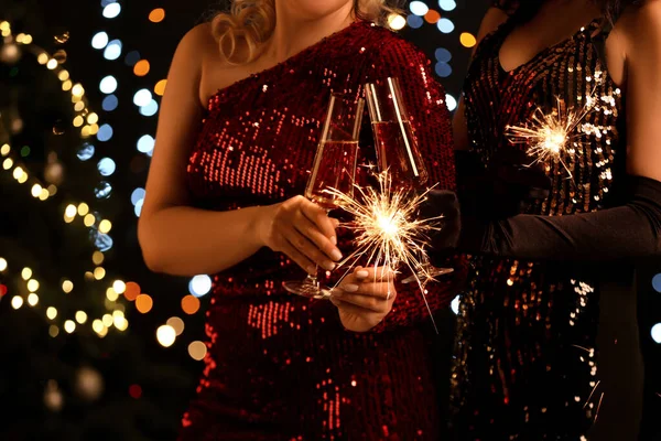 Жінки Елегантних Сукнях Палаючими Блискітками Келихами Шампанського Проти Розмитих Різдвяних — стокове фото
