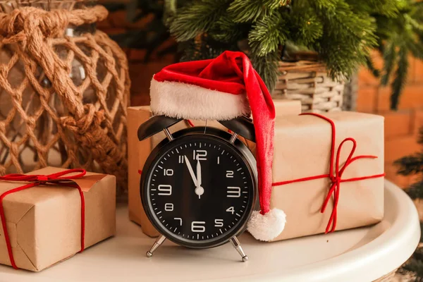 サンタの帽子とクリスマスプレゼント付き目覚まし時計は 部屋のテーブルの上で クローズアップ — ストック写真