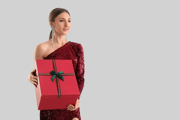 stock image Young woman in red dress with Christmas gift on grey background