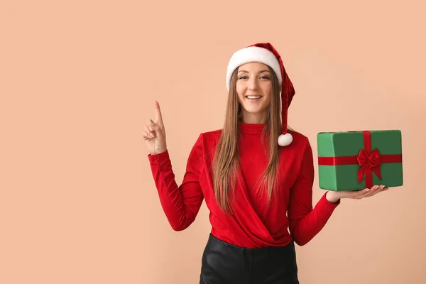 Young Woman Santa Hat Christmas Gift Pointing Something Beige Background — Stock Photo, Image