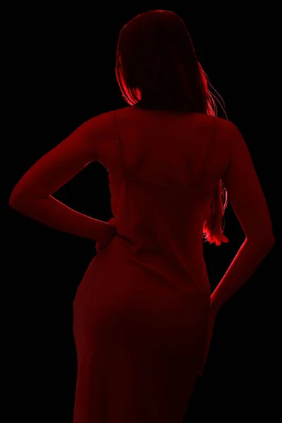 Silhouette of young woman in silky dress on black background, back view