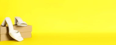 Sarı zemin üzerinde karton kutu ve beyaz sandaletler ve metin için boşluk